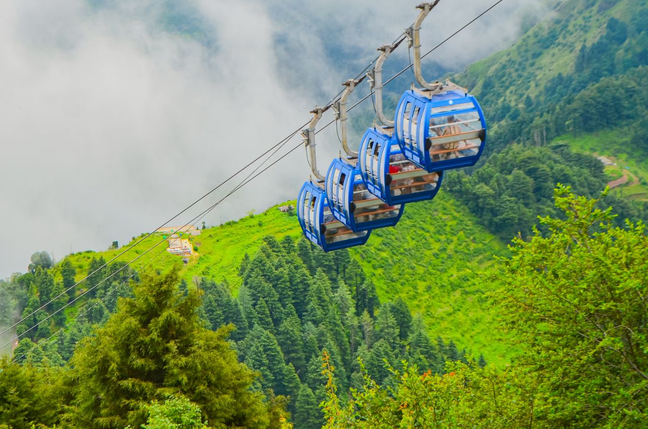 Breathtaking view of cable cars gliding over lush green mountainous landscape with mist.